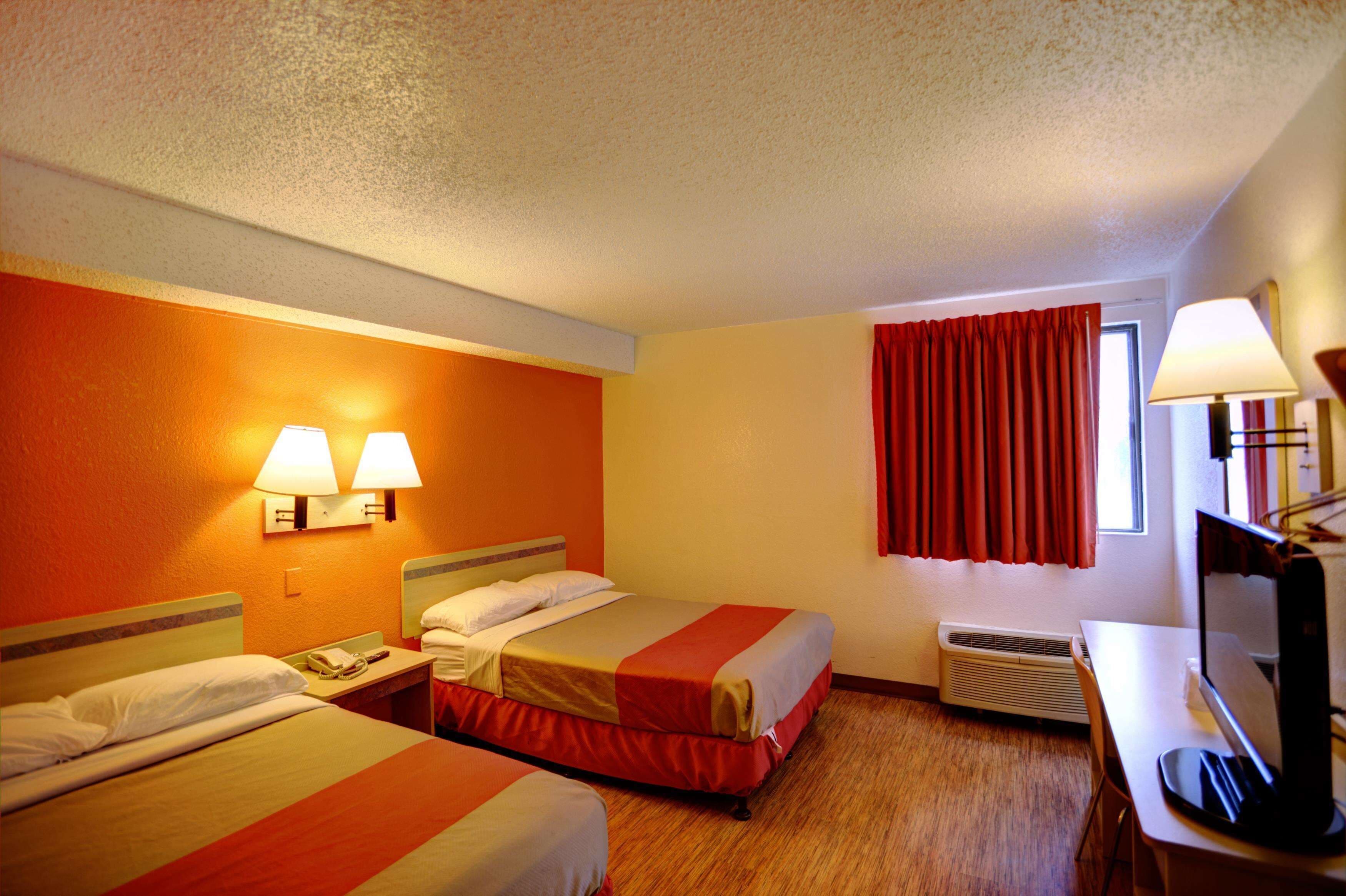 A hotel room with two beds, a desk, a chair, a television, a lamp, and a window with curtains.