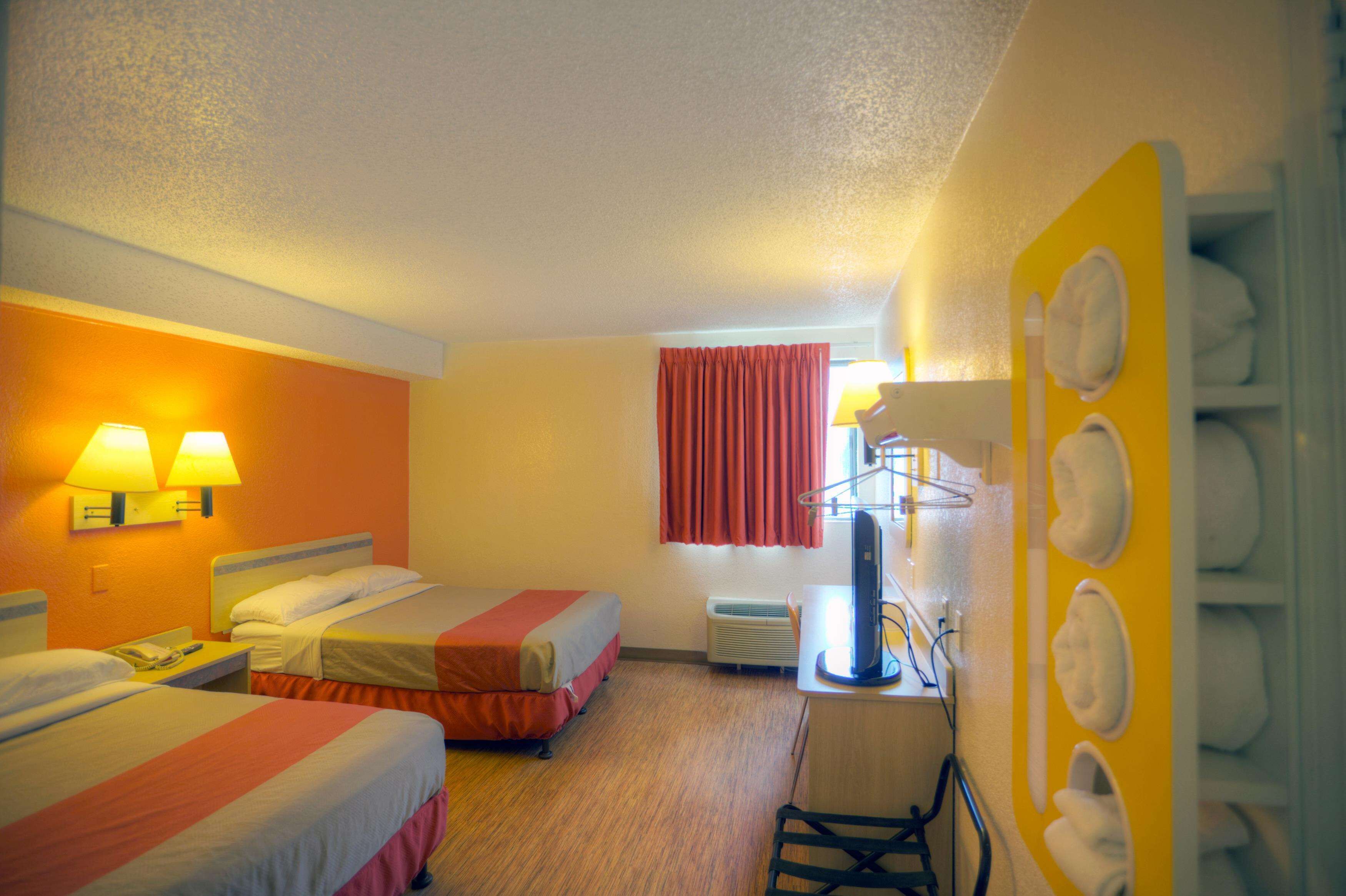 Een hotelkamer met twee bedden, een bureau, een stoel, een telefoon en een wandheater.