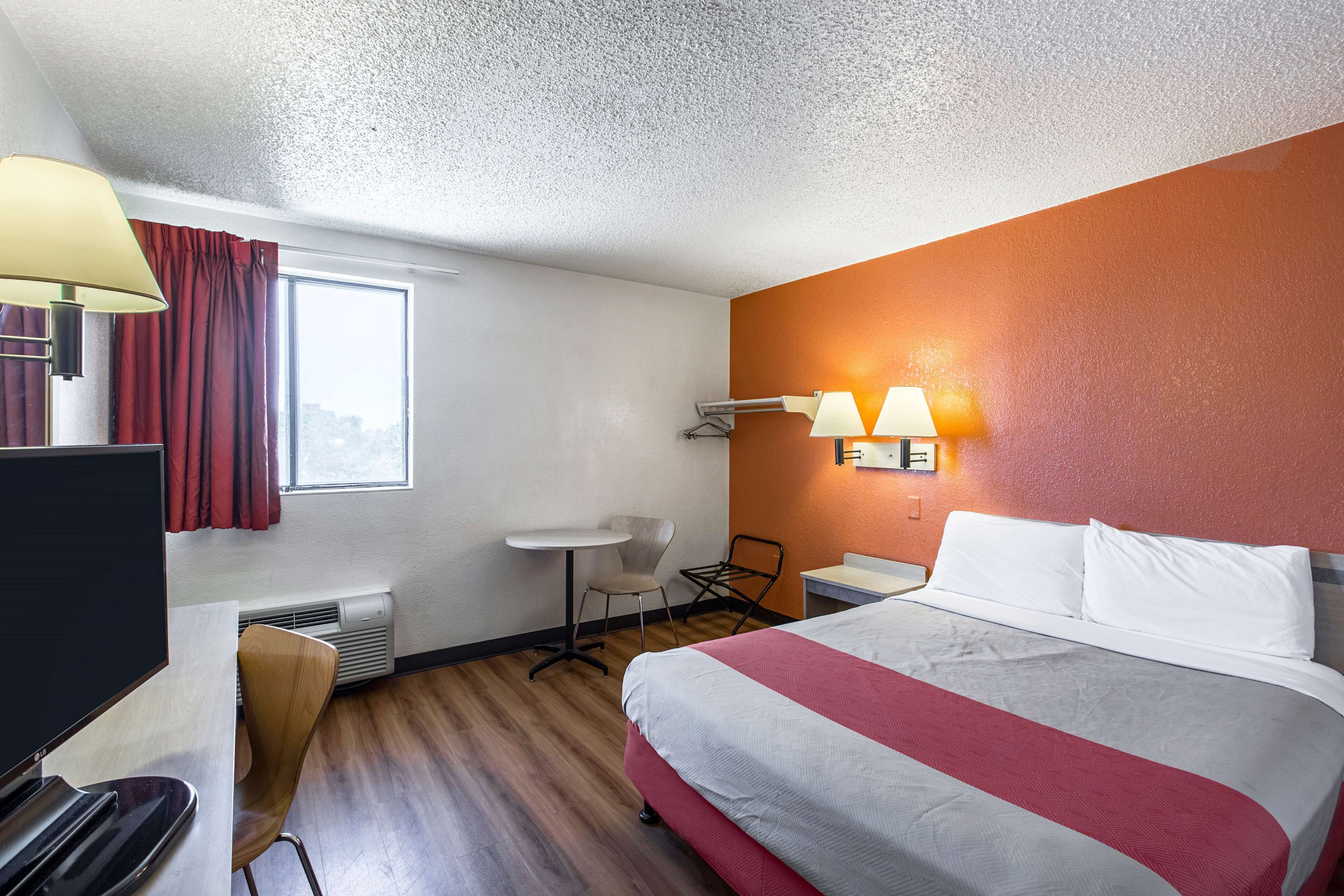 A hotel room with a bed, a desk, a chair, a TV, and a window with curtains.