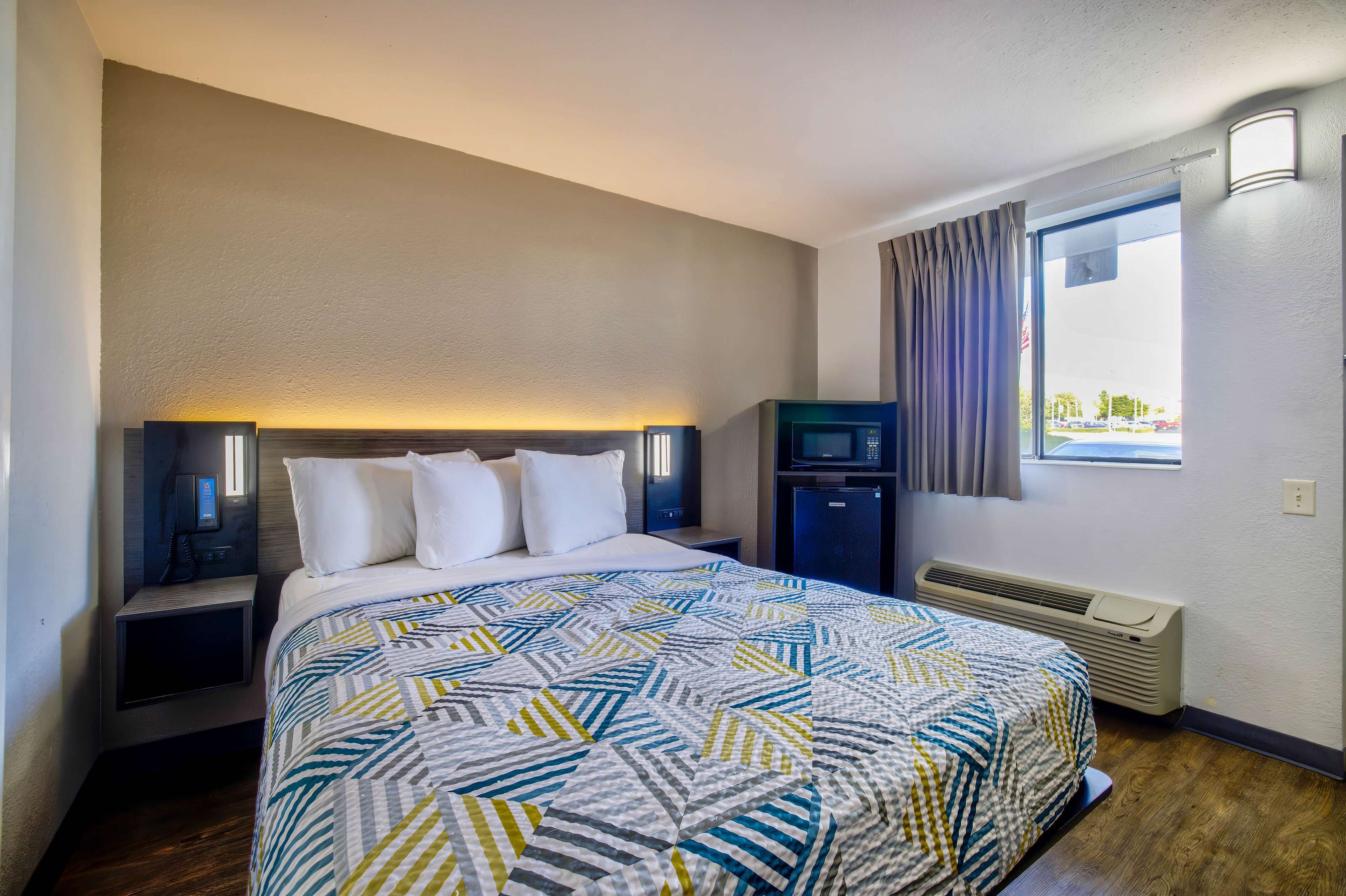 A hotel room with a bed, nightstands, a TV, a heater, and a window with curtains.