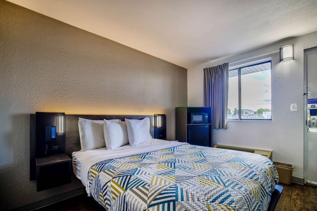 A hotel room with a bed, nightstand, wall-mounted TV, and a window with curtains.
