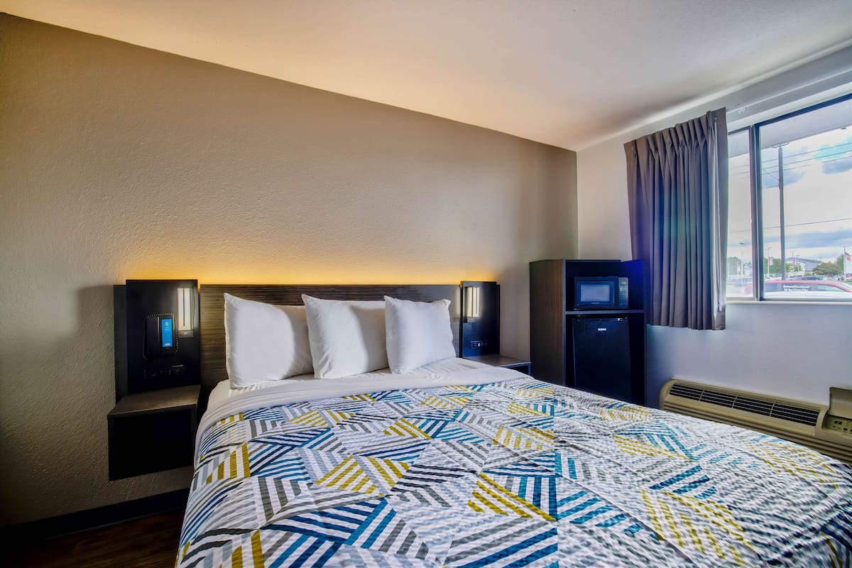 A hotel room with a bed, bedside tables, a heater, and a window with curtains.