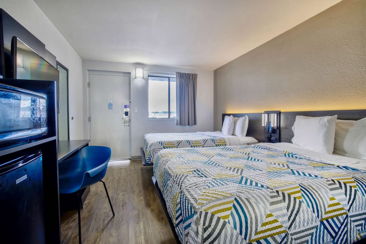 A hotel room with two beds, a desk with a television, and a window with curtains.