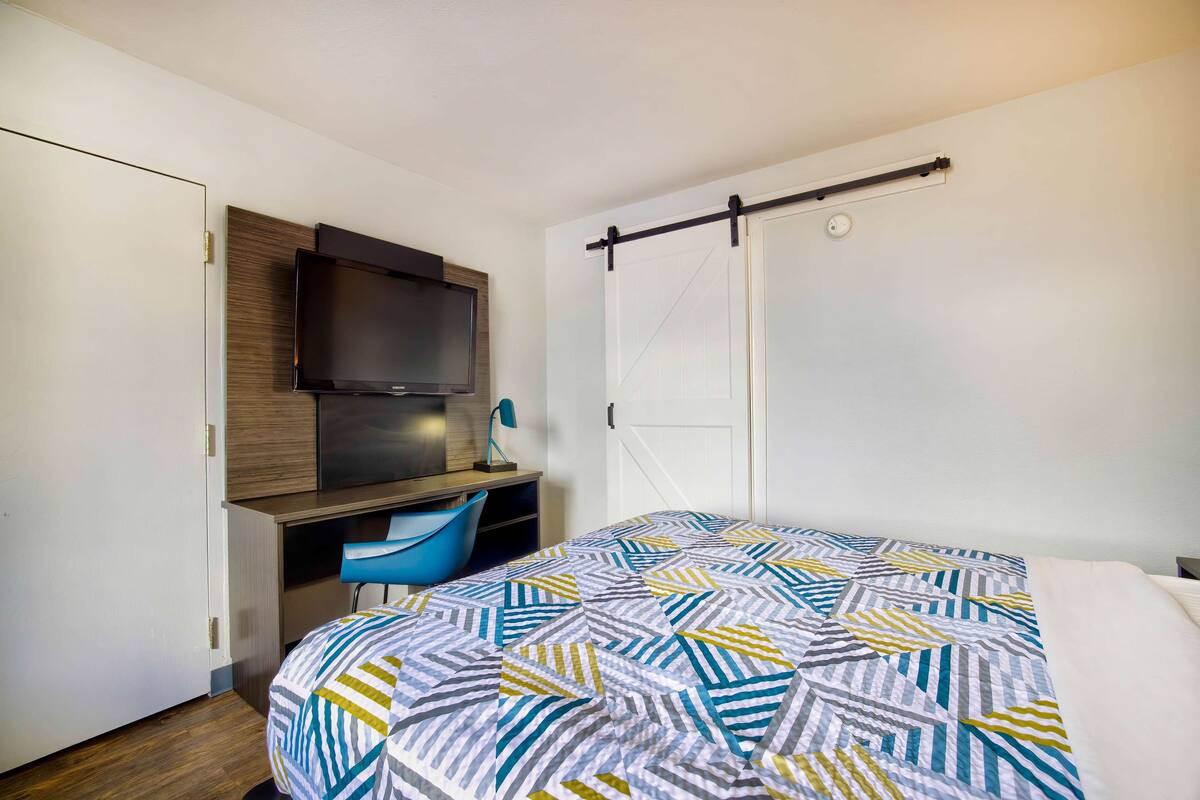 A bedroom with a bed, a desk, a chair, a TV mounted on the wall, and a sliding door.