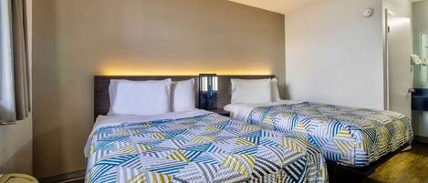 Habitación de hotel con dos camas, cada una con ropa de cama estampada, una lámpara de pared sobre las camas y una mesita de noche pequeña.