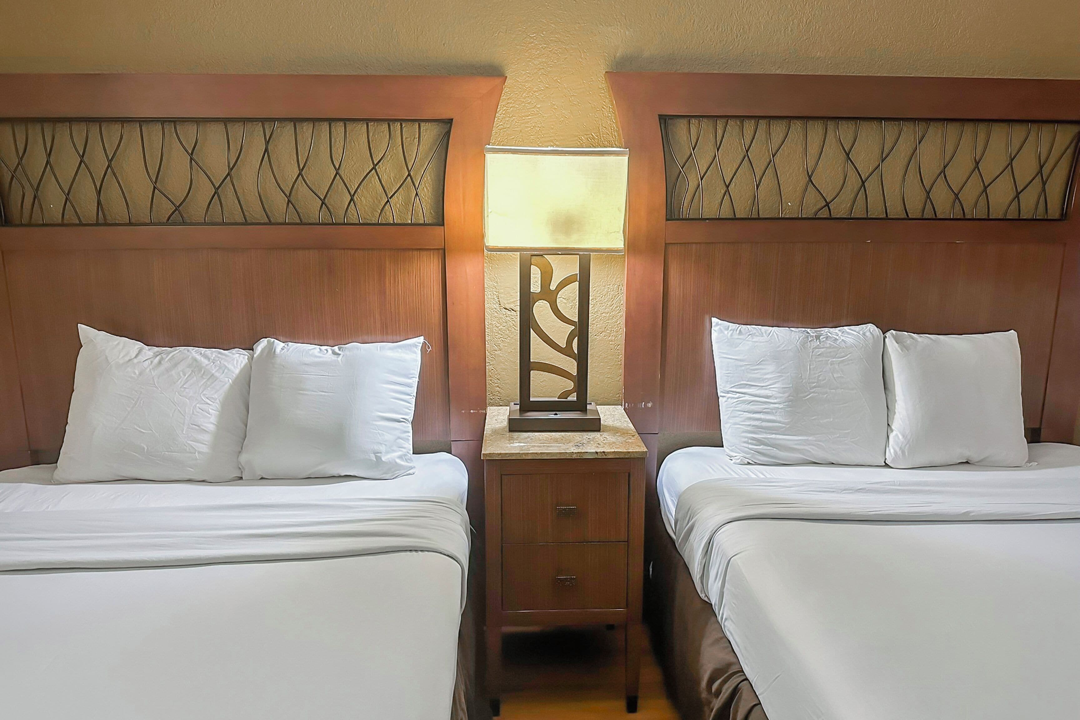 A hotel room with two beds, a nightstand with a lamp, and a decorative wall panel.