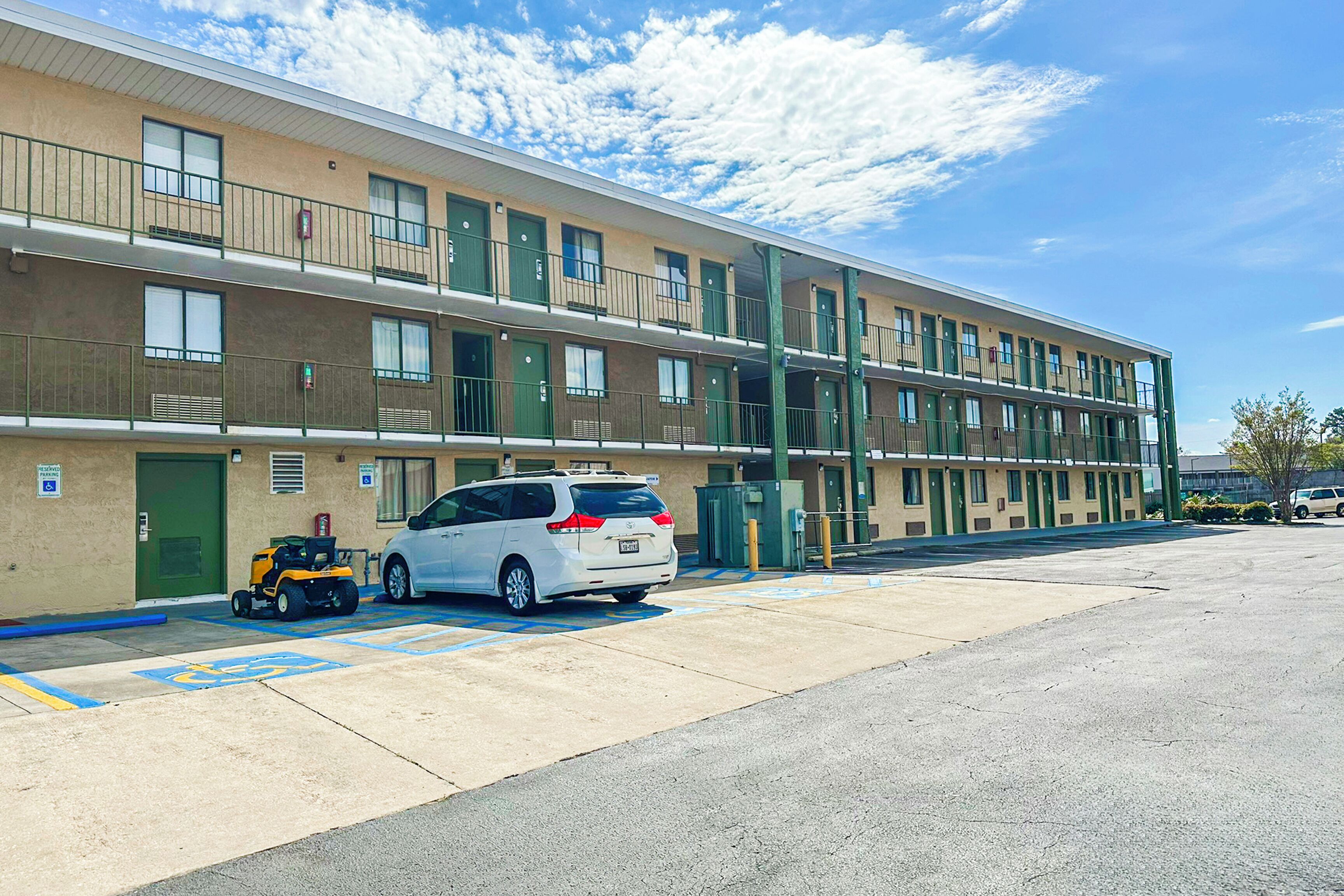 A multi-story motel with a parking lot, a white car, and a golf cart.