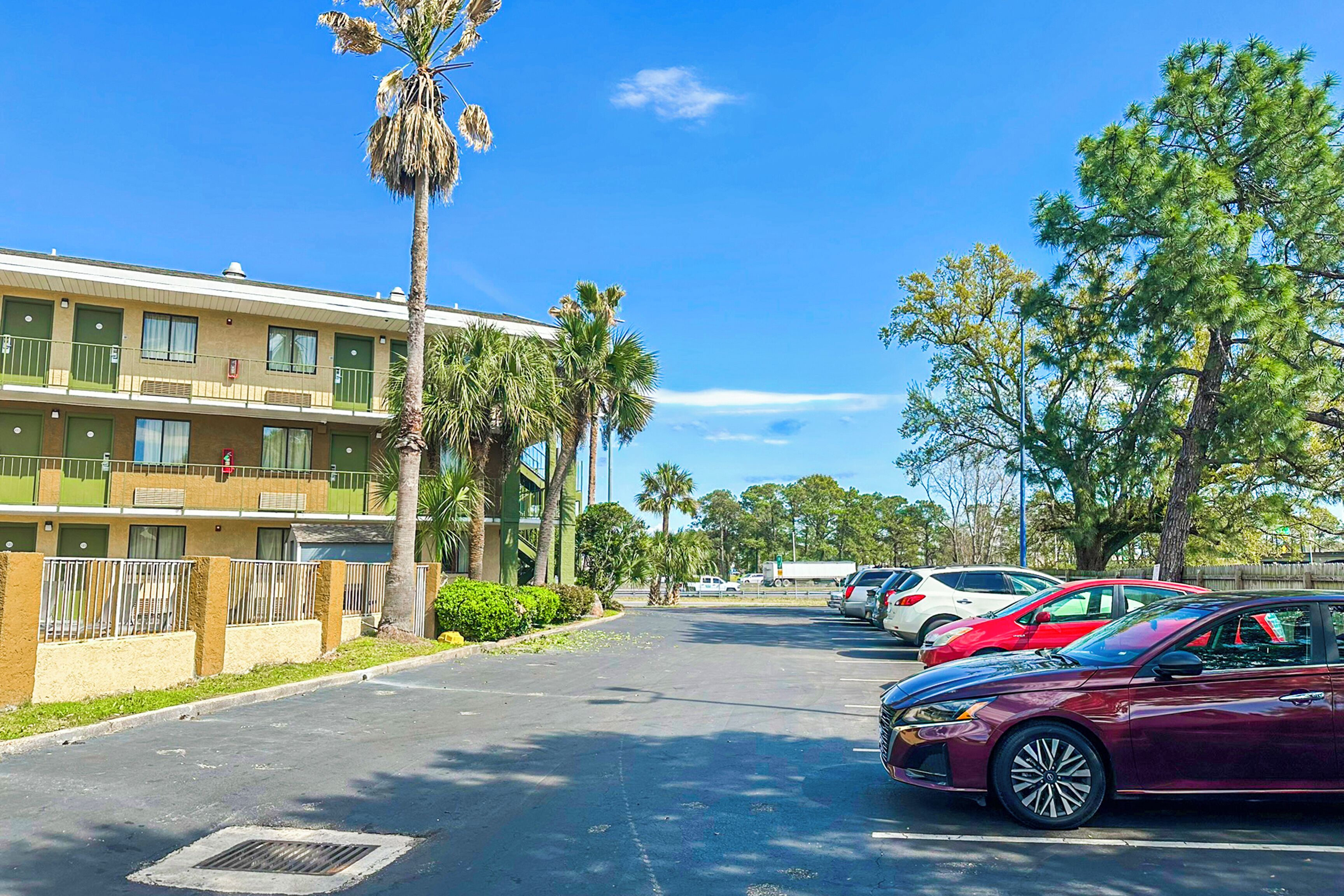 Un hotel a più piani con balconi, palme e auto parcheggiate.