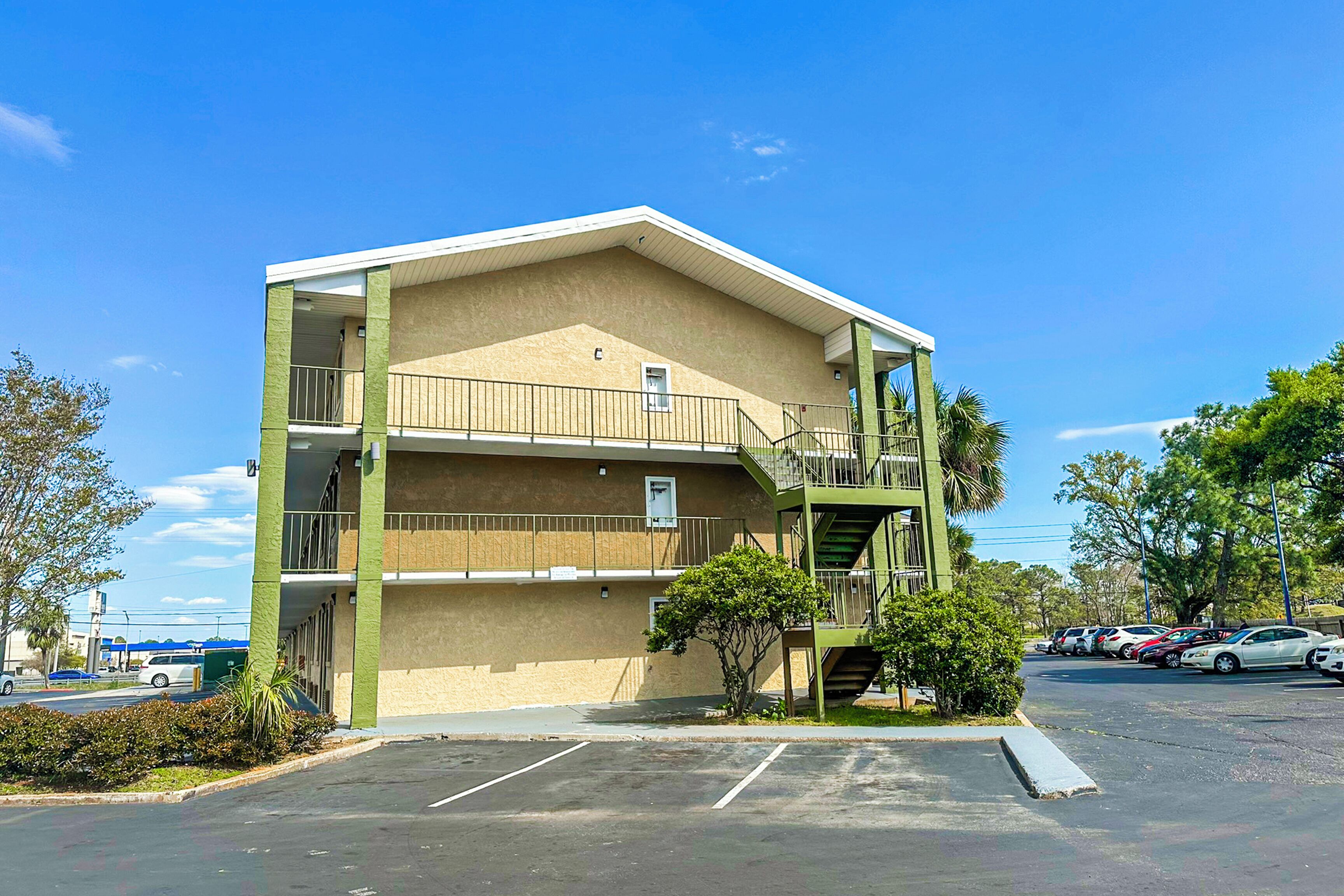 A two-story building with a flat roof and a green exterior. There is a parking lot in front with several cars parked.