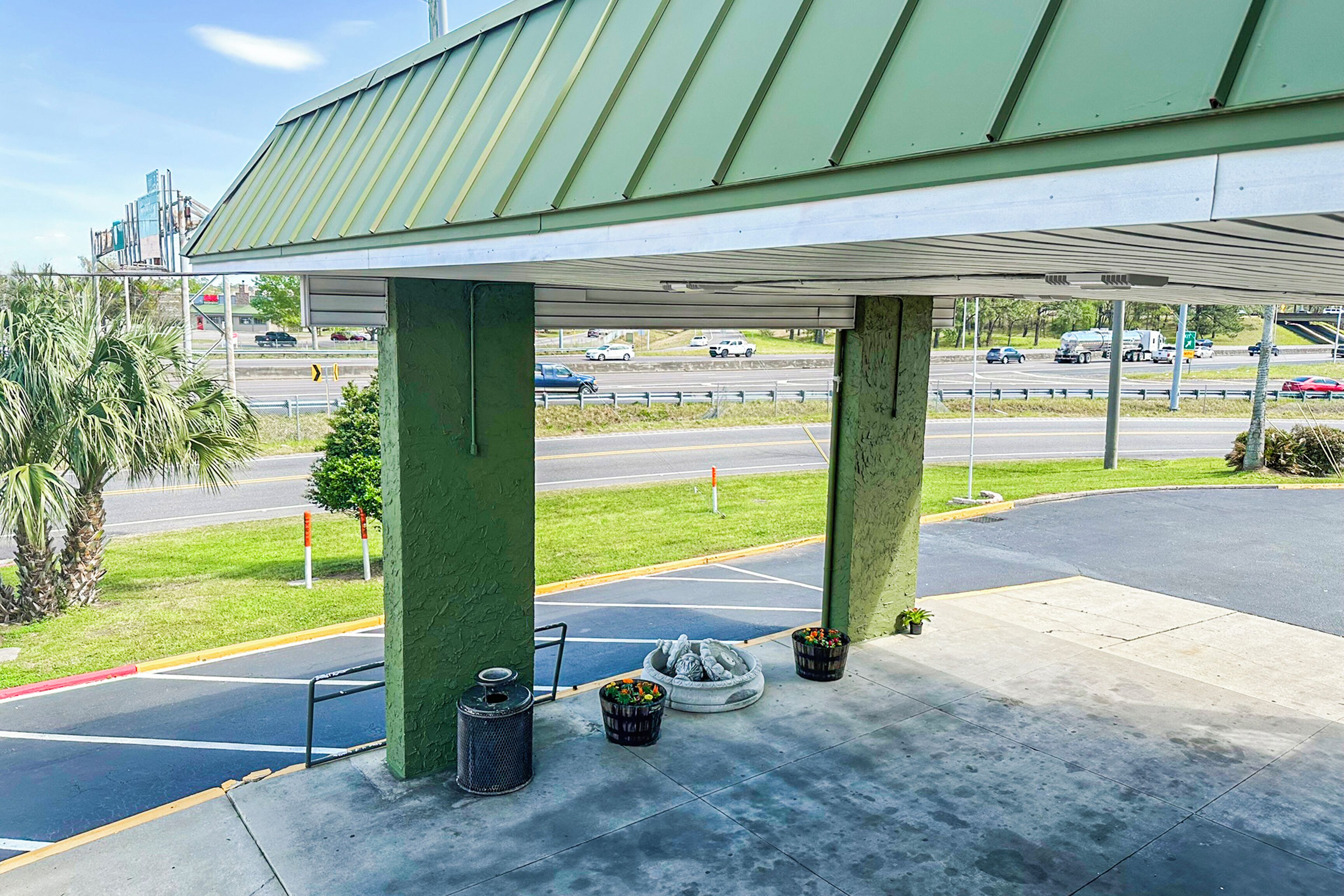 Una estación de servicio con techo verde, zona de espera cubierta y vistas a la autopista.