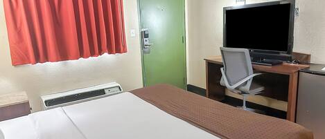 A hotel room with a bed, a desk with a television, a chair, and a green door.
