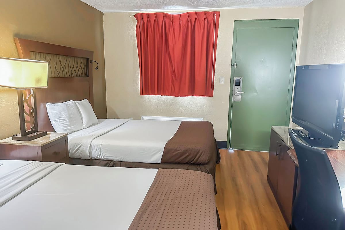 Una habitación de hotel con dos camas, un escritorio con televisor, una puerta verde y una cortina roja.