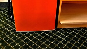 A compact orange refrigerator with a small logo, placed next to a wooden table with multiple drawers. - QC Stay Inn (Moline)