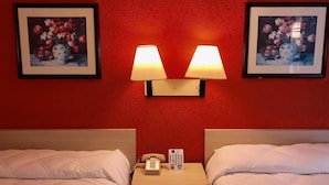 A hotel room with two beds, a nightstand with a phone and a sign, and two wall-mounted lamps. - QC Stay Inn (Moline)
