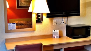 A hotel room with a bed, a desk with a chair, a television, a microwave, and a trash can. - QC Stay Inn (Moline)
