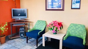 A reception area with two green upholstered chairs, a small table with a vase of flowers, a desktop computer, and a television on a stand. - QC Stay Inn (Moline)