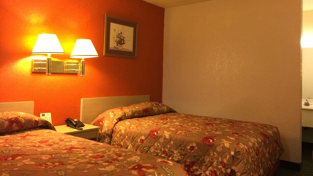 A hotel room with two beds, each with floral bedding, a nightstand with a phone, and wall-mounted lamps. - QC Stay Inn (Moline)