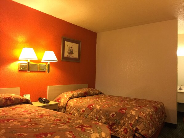 A hotel room with two beds, each with floral bedding, a nightstand with a phone, and wall-mounted lamps.