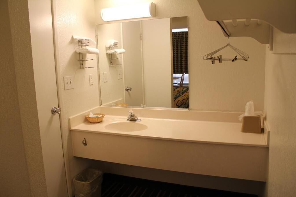 Une salle de bain d’hôtel équipée d’un lavabo, d’un miroir, d’un porte-serviettes et d’un étendoir à vêtements.