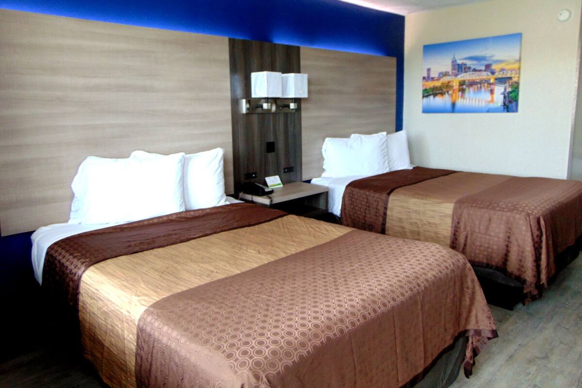 A hotel room with two beds, a nightstand with a lamp, and a painting on the wall.