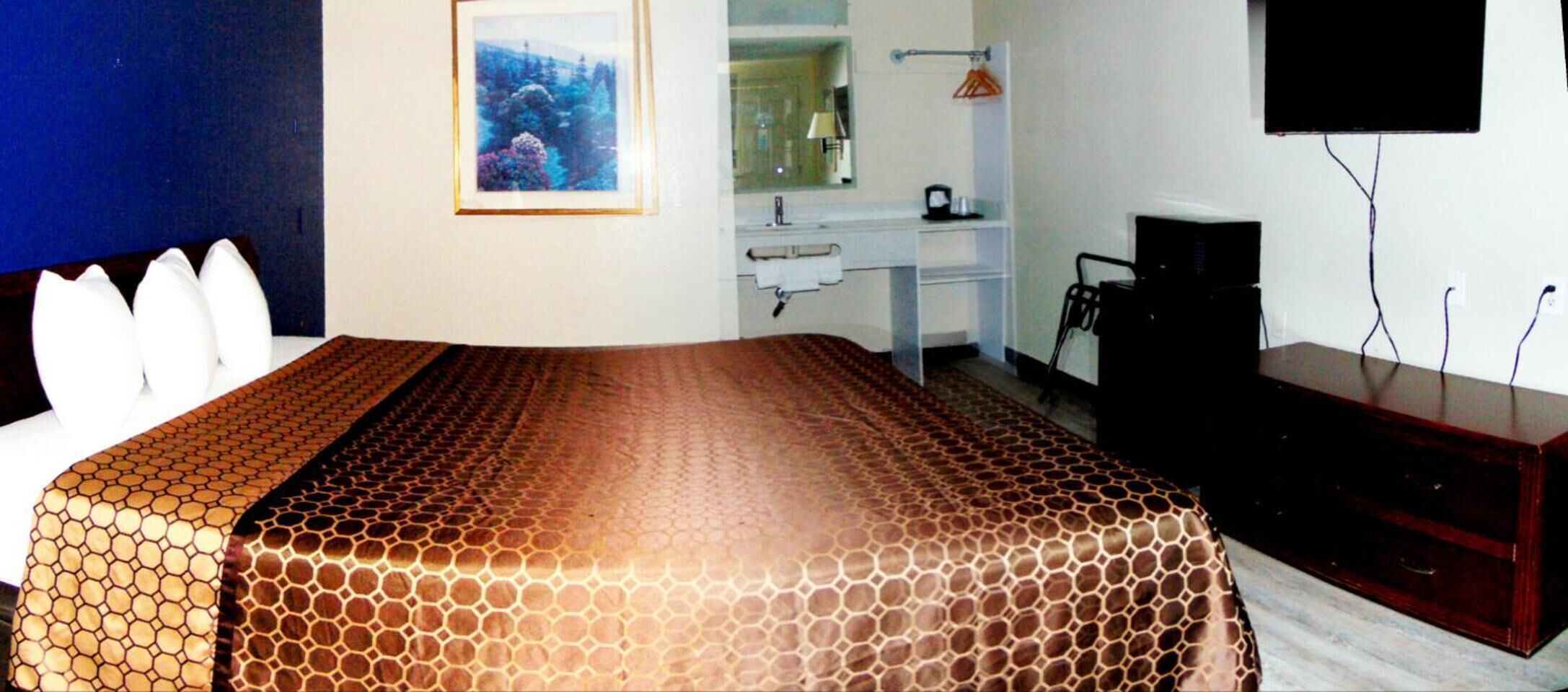 A hotel room with a bed, a desk, a chair, a television, and a mirror.