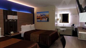 Habitación de hotel con dos camas, un escritorio, un espejo, una ventana y un cuadro en la pared.