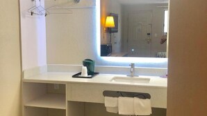 A small bathroom with a white sink, a mirror, a towel rack, and a trash bin. - Somatel Nashville Airport Hotel (Nashville)