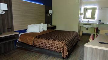 Une chambre d’hôtel comprenant un lit, un bureau, une chaise, un miroir et une salle de bain avec un lavabo et des toilettes.