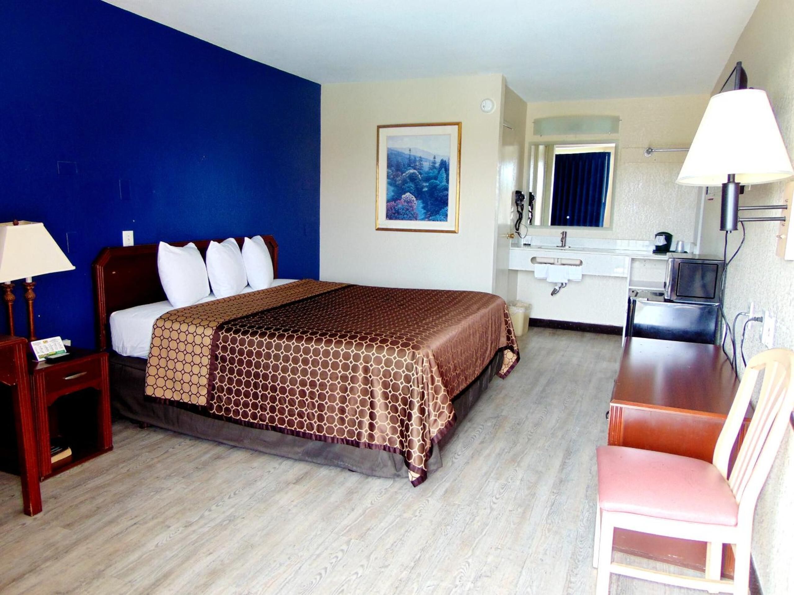 Ein Hotelzimmer mit Bett, Schreibtisch, Stuhl, Spiegel und einem Bild an der Wand.