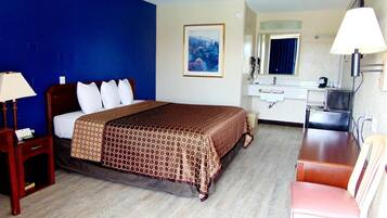 A hotel room with a bed, a desk, a chair, a mirror, and a painting on the wall.