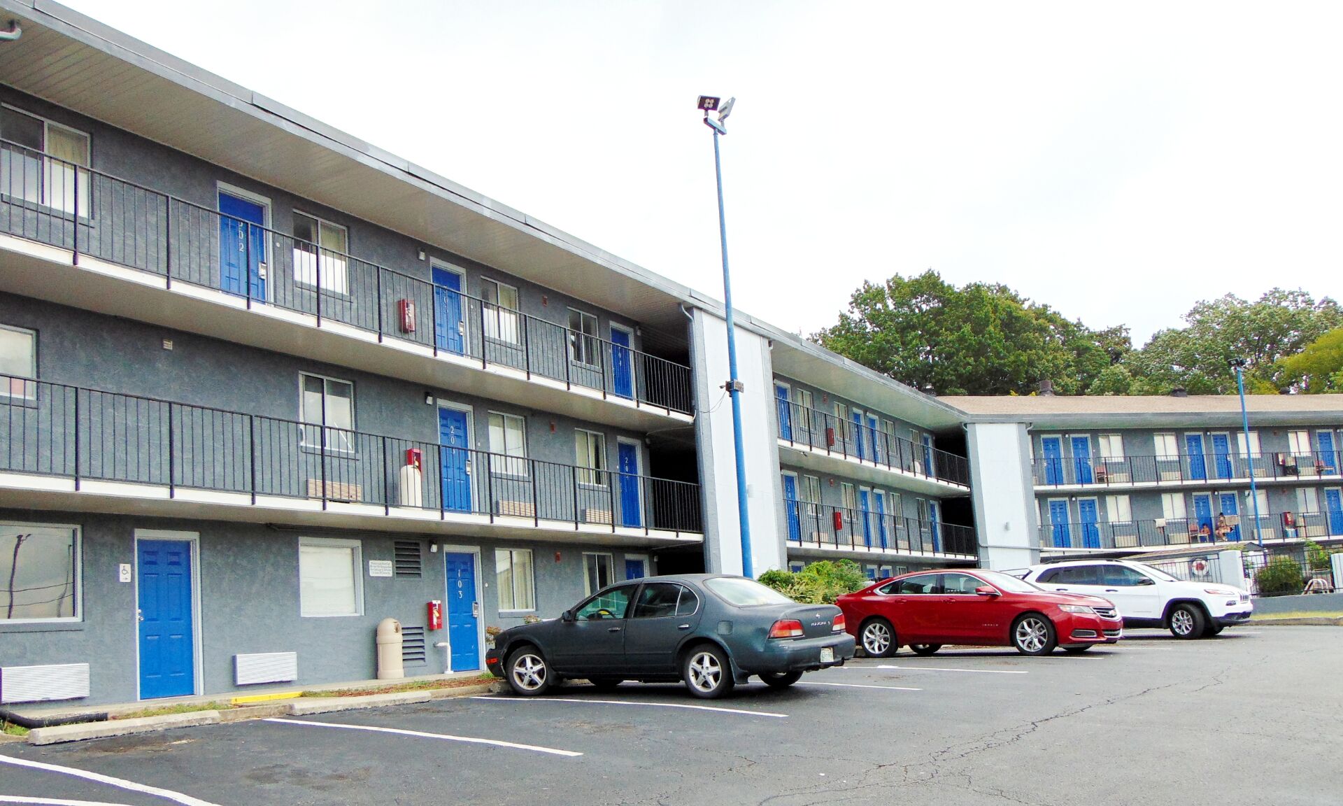 A multi-story motel with blue doors and balconies, featuring a parking lot with several cars.