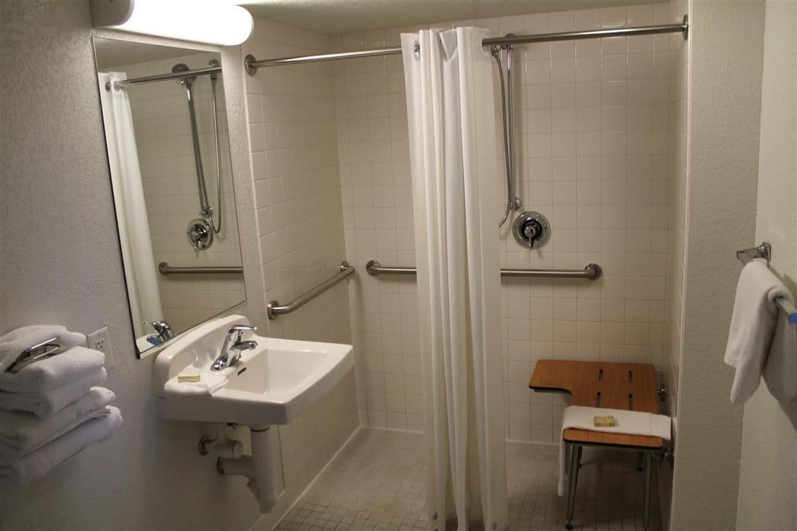 A bathroom with a sink, mirror, shower, and grab bars.