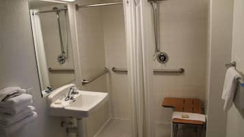 A bathroom with a sink, mirror, shower, and grab bars.