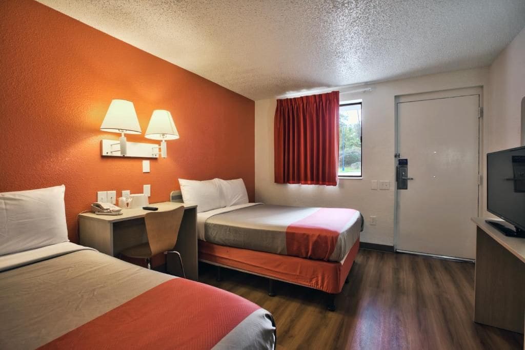A hotel room with two beds, a desk with a telephone, and a television.