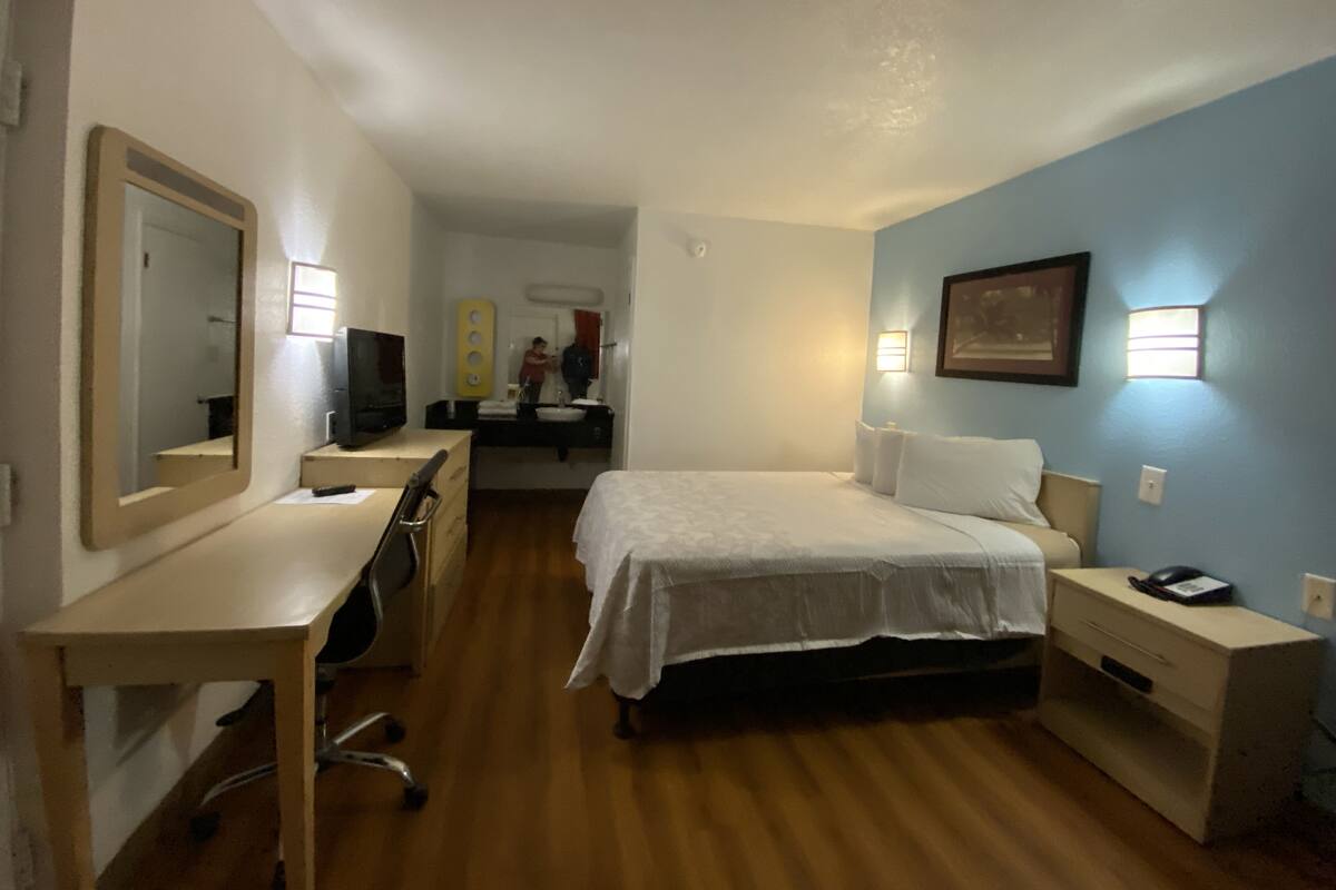 A hotel room with a bed, bedside table, desk, chair, and a mirror.