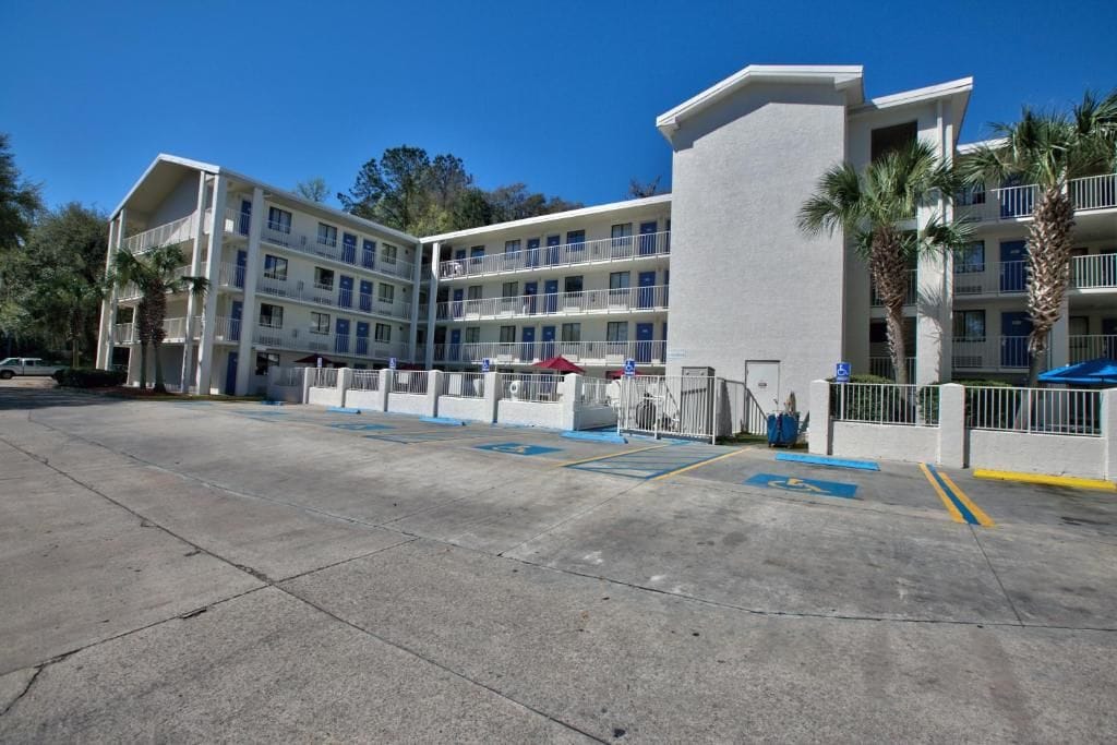A multi-story hotel with a parking lot, a covered area, and a building with balconies.