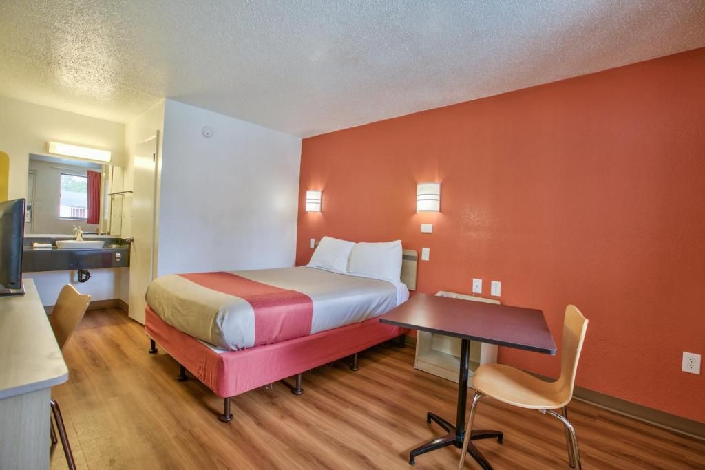 A hotel room with a bed, a desk, a chair, a television, and two wall-mounted lights.