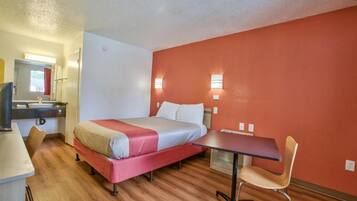 A hotel room with a bed, a desk, a chair, a television, and two wall-mounted lights.