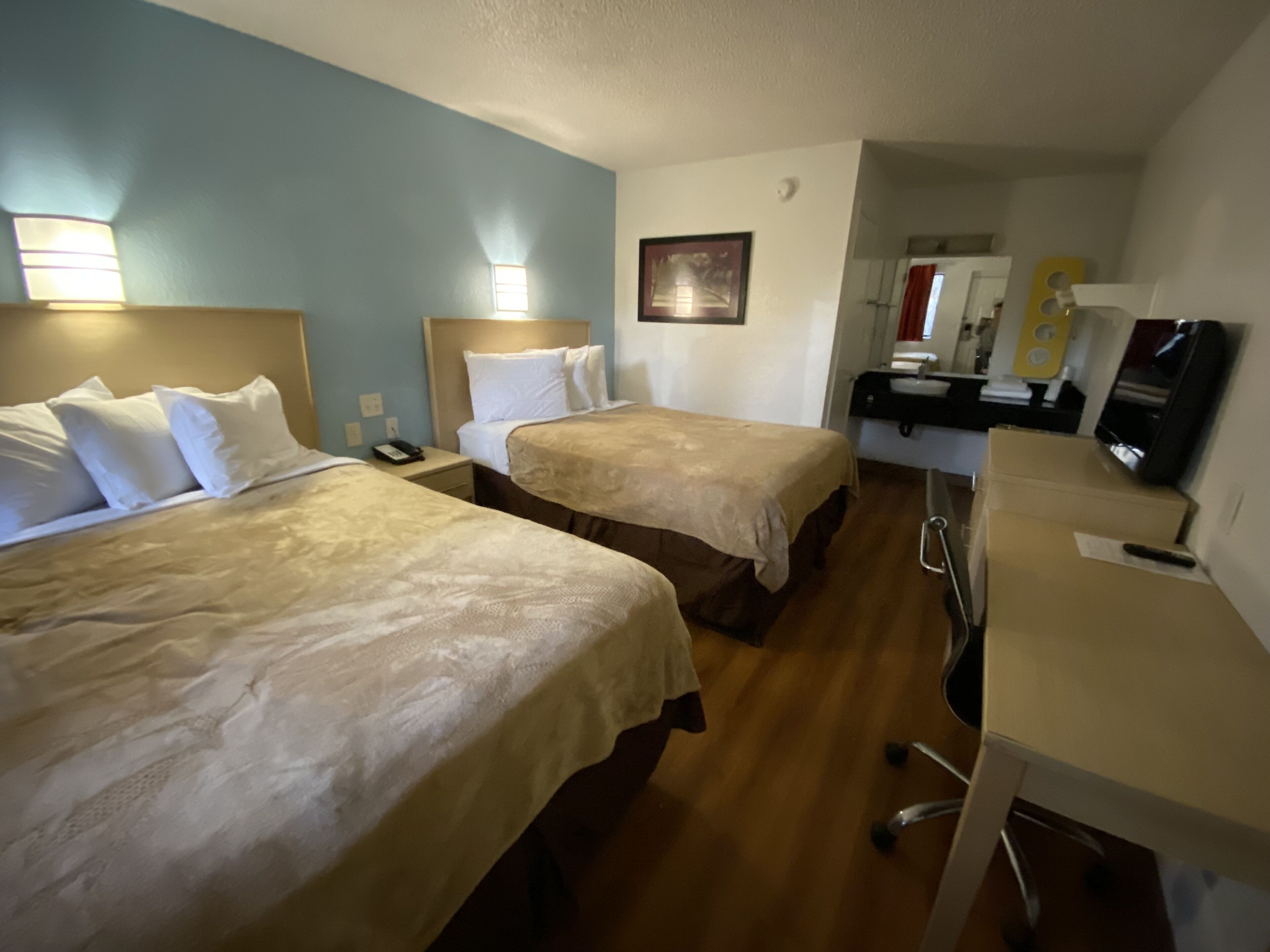 A hotel room with two beds, a desk, a chair, a mirror, and a television.