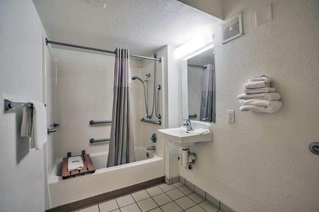 Une salle de bain équipée d’une baignoire, d’une douche et d’un lavabo, ainsi que de barres d’appui et d’un porte-serviettes.