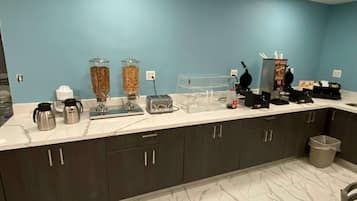 Una cocina con encimera de mármol, dos cafeteras, un tostador, una licuadora y un cubo de basura.