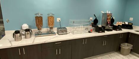Una cocina con encimera de mármol, dos cafeteras, un tostador, una licuadora y un cubo de basura.