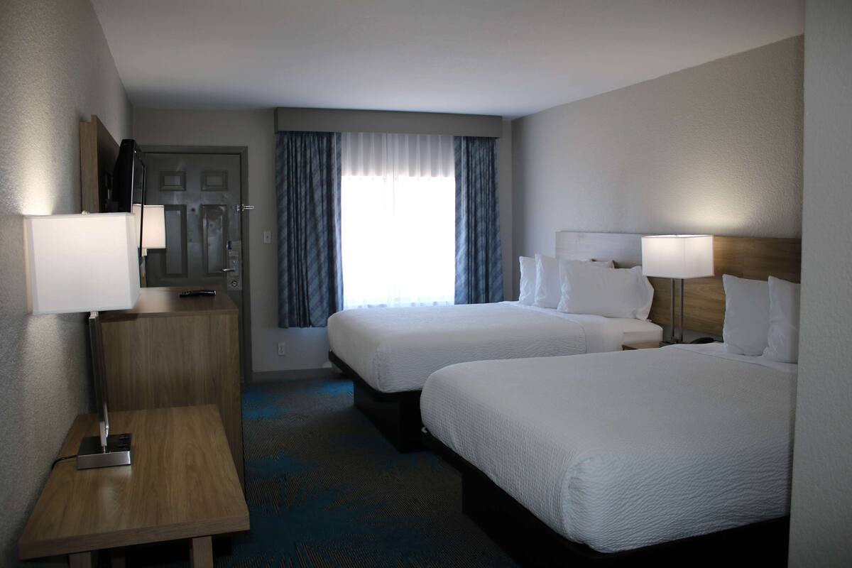 Une chambre d’hôtel avec deux lits, un bureau, une lampe et une fenêtre avec des rideaux.
