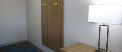 Una habitación con un armario de madera, una mesita con lámpara y una alfombra azul estampada.