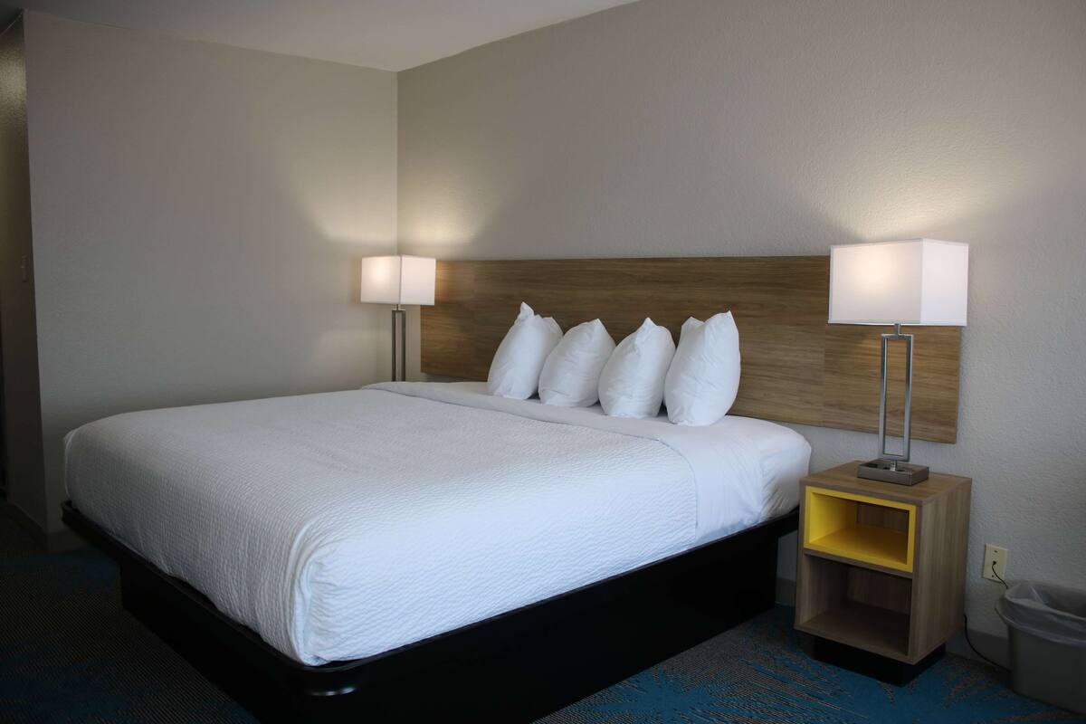 Une chambre d’hôtel avec un grand lit, deux lampes de chevet, une tête de lit en bois et une petite table de chevet en bois avec une étagère jaune.