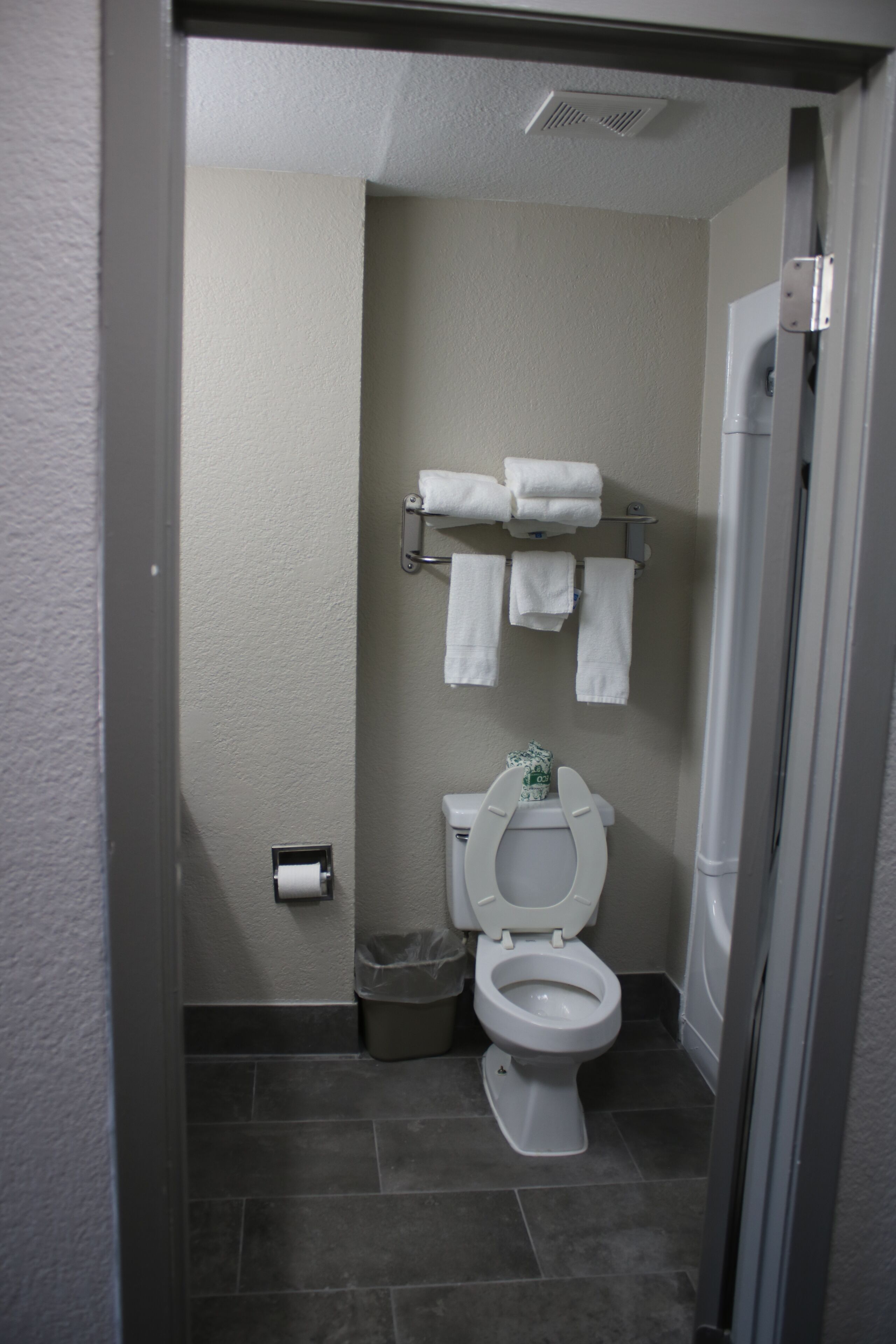 Un baño con inodoro, toallero con varias toallas, cubo de basura y zona de ducha.