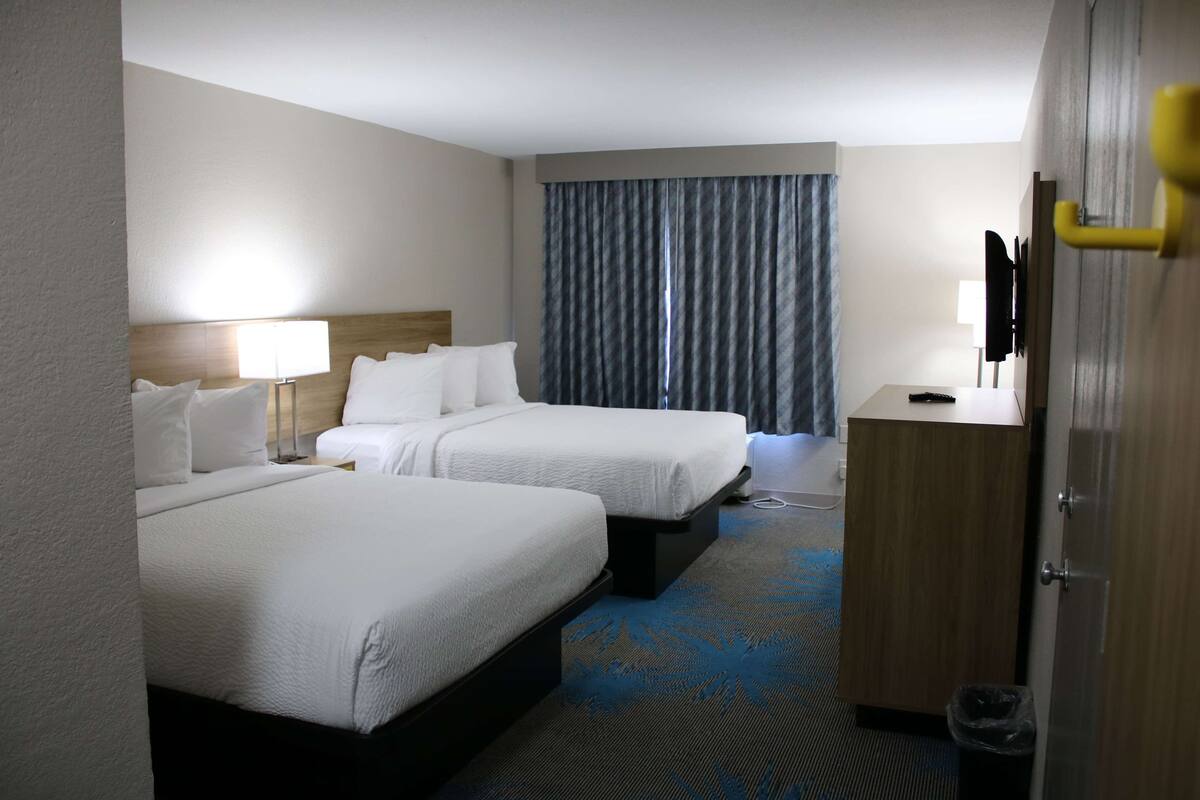 Une chambre d’hôtel avec deux lits, un bureau, une chaise, une lampe, une télévision et une armoire.