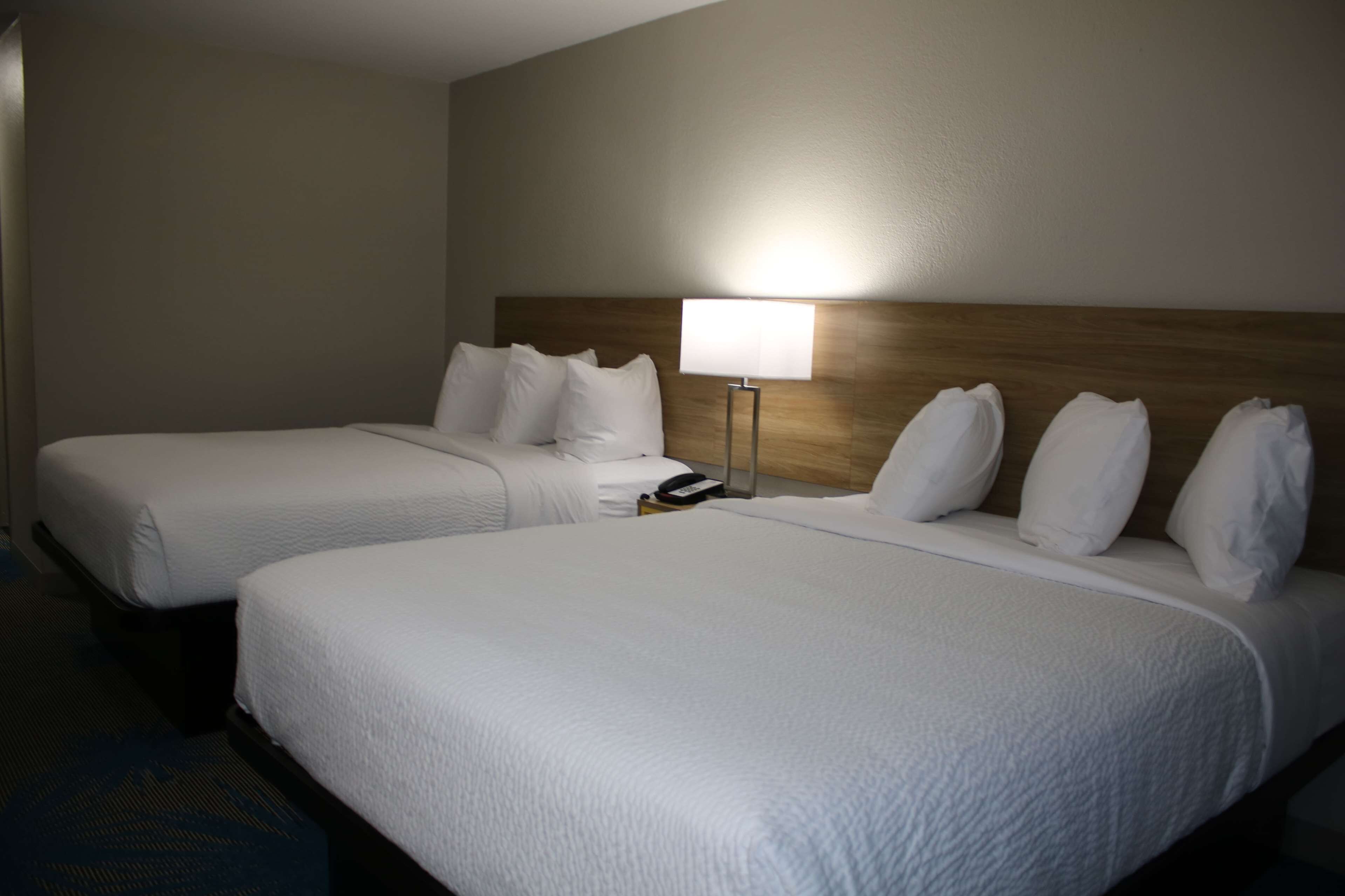 A hotel room with two beds, a nightstand with a lamp, and a wooden headboard.