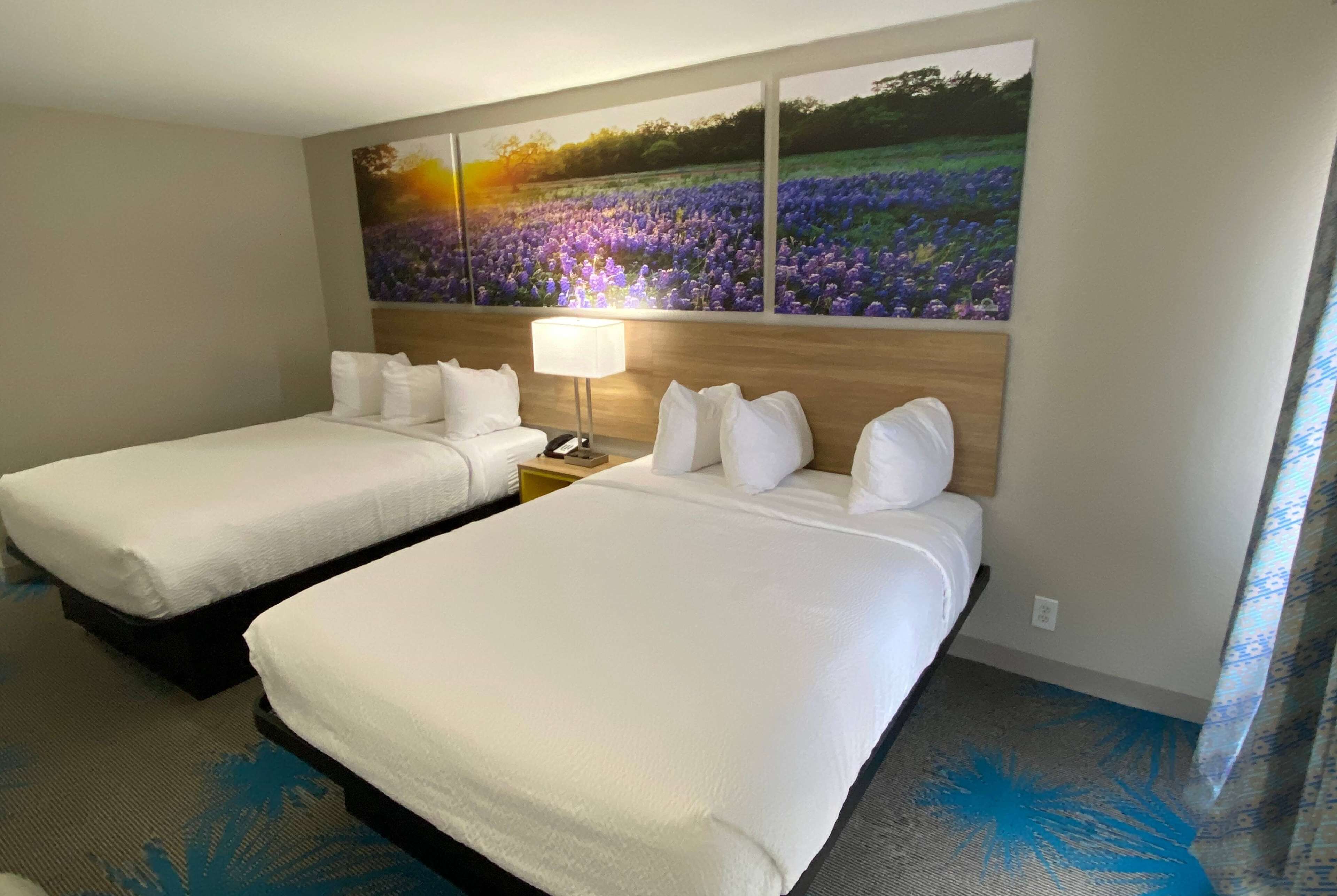 Une chambre d’hôtel avec deux lits, une table de chevet avec une lampe et un grand tableau représentant des fleurs accroché au mur.