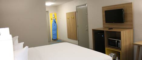 Habitación de hotel con cama, televisor montado en la pared, microondas en un mueble de madera y puerta que da a otra habitación.